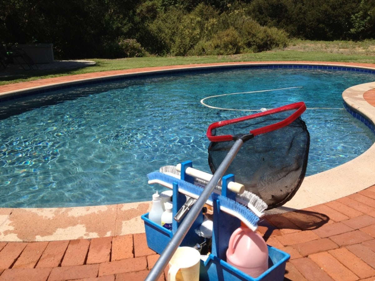 Pool startup gear on a brick patio beside a clean residential swimming pool